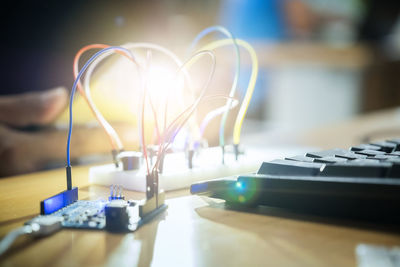 Close-up of computer keyboard with illuminated electrical equipment on wooden table