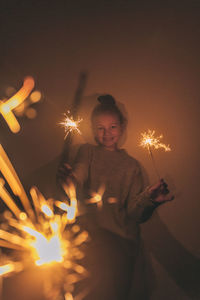 Girl making with sparkler in darkroom against wall