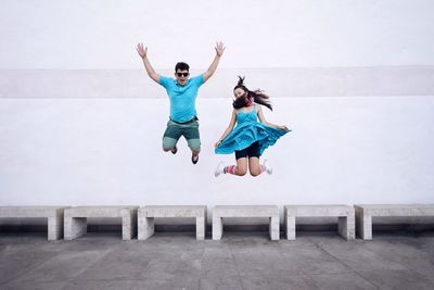 Playful friends jumping against white wall