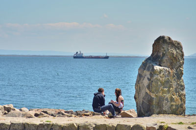 People sitting on rock by sea against sky