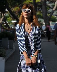 Young woman wearing sunglasses walking on sidewalk in city