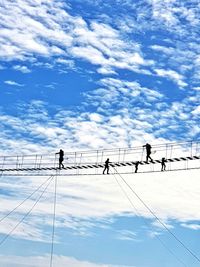 Low angle view of people on cable against sky