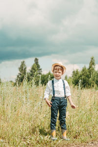 Little farmer on a summer field, cute little boy in a straw hat. boy with a flower stands 