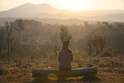 Rear view of man sitting on land against mountains