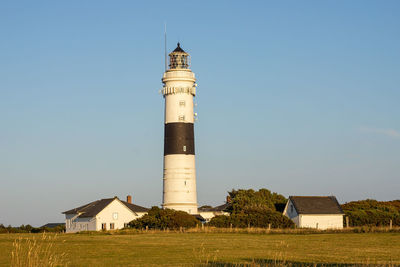 Lighthouse on field by building against sky