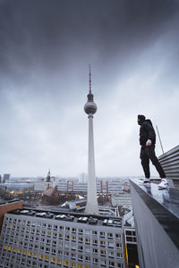 Low angle view of young man standing on building against cloudy sky