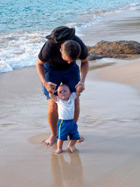 Full length of father with baby boy standing on shore at beach