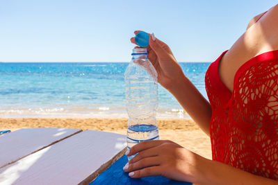 Close-up of a girl opening a plastic water bottle after swimming in the sea.