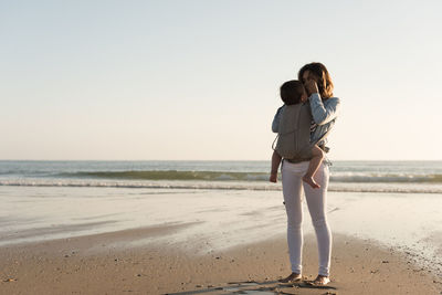 Mother carrying son while standing at beach