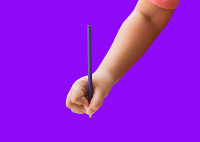 Close-up of hand holding purple flower against blue background