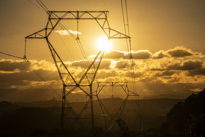 Low angle view of electricity pylon against sky during sunset