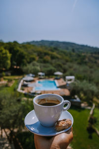 Cropped hand of woman holding coffee cup against sky