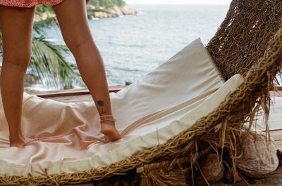 Low section of woman standing on hammock against sea