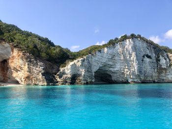 Rock formation by sea against blue sky