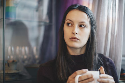 Young woman holding coffee cup in college dorm room