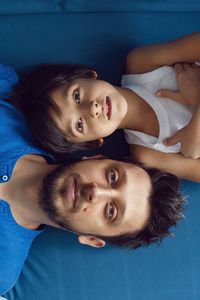 Portrait of a family father and son sitting on a blue sofa in the studio opposite the window. 