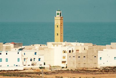 Lighthouse by sea against clear blue sky