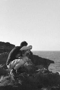 Man on rock by sea against clear sky