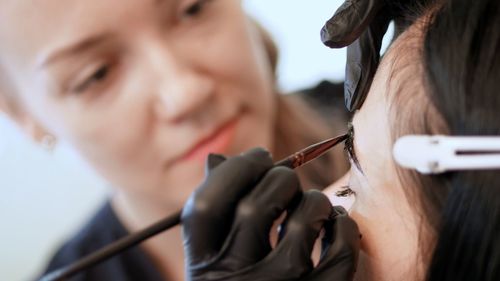 Young woman gets eyebrow correction procedure. kosmetolog- makeup artist in black rubber gloves 