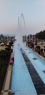 People at fountain in city against clear sky