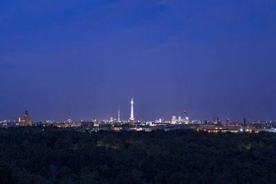 Illuminated city against clear blue sky at night