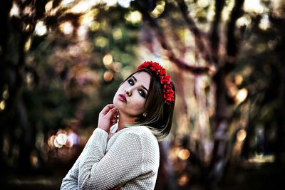 Side view portrait of young woman wearing red flowers against trees