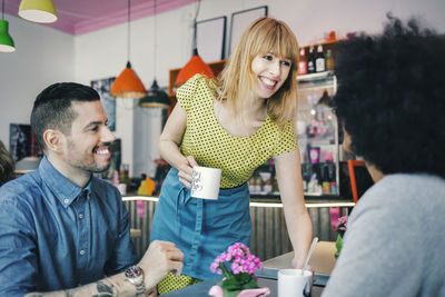 Woman serving coffee to customers in cafe