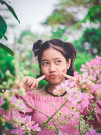 Girl touching cheeks while standing by flowering plants