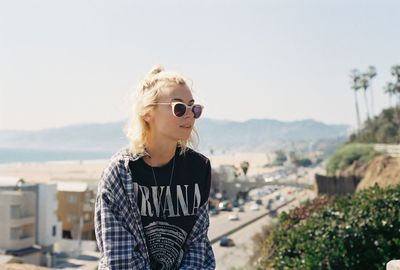 Young woman wearing sunglasses standing in city against sky