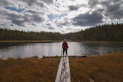 Explorer in a red and black shirt and grey cap stands on edge of a wooden walkway enjoying the view 