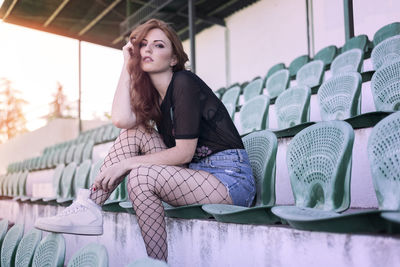 Portrait of young woman sitting on chair at stadium