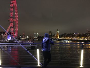 Rear view of standing on bridge over river at night