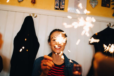 Cheerful young woman holding sparkler while enjoying dinner party at restaurant