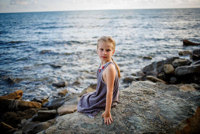 Portrait of boy sitting on rock at sea shore