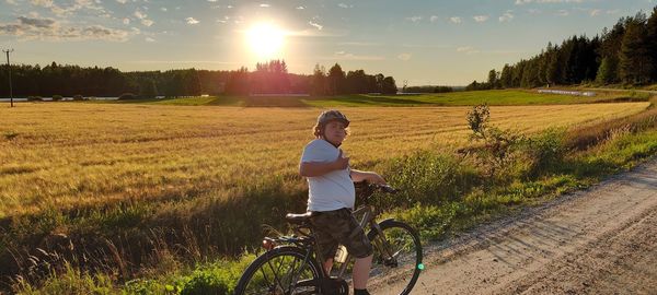 Man riding bicycle on field against sky during sunset