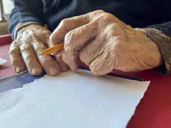 Writing, closeup wrinkled hands of old person holding a pen to write on blank or empty white paper. 