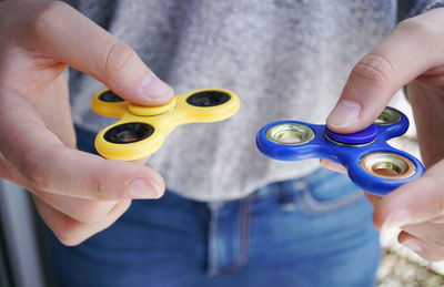 Midsection of women holding yellow and blue fidget spinners