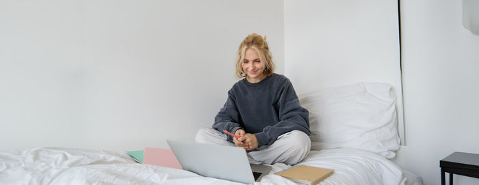 Portrait of young woman using laptop while lying on bed at home