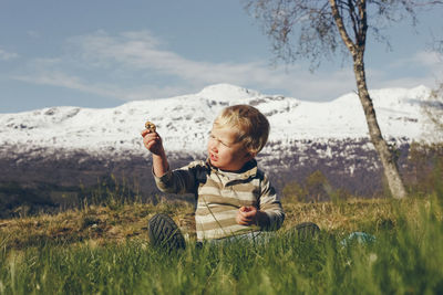 Cute boy holding stone while sitting on grassy land