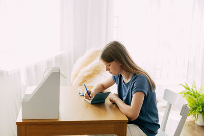 A smart teenage schoolgirl makes notes in a notebook for homework or an exam, recreates the material