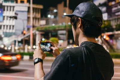 Rear view of man photographing through phone on road at night
