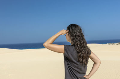 Rear view of woman standing on beach against clear blue sky