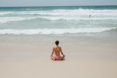 Rear view of woman in bikini meditating at beach