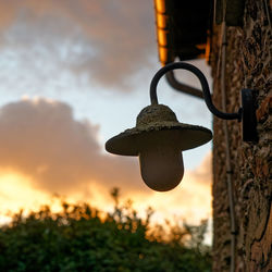 Close-up of electric lamp hanging against sky at sunset