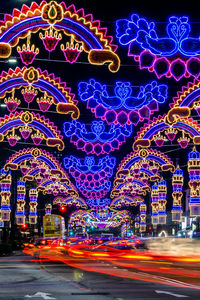 Illuminated christmas lights on road by building at night