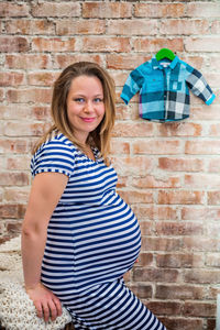 Portrait of smiling pregnant woman standing against brick wall
