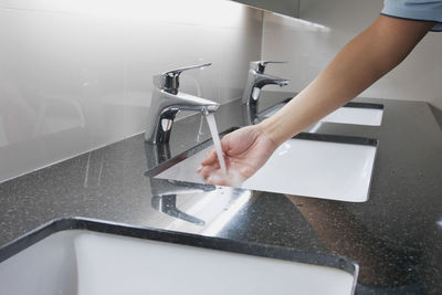 Cropped hand of woman washing hand in bathroom sink
