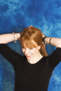 Smiling young woman tying hair while standing against blue background