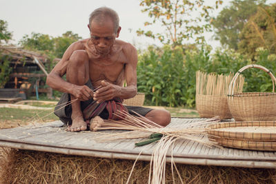 Shirtless senior man making straw basket