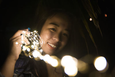 Portrait of smiling woman holding illuminated lights at night